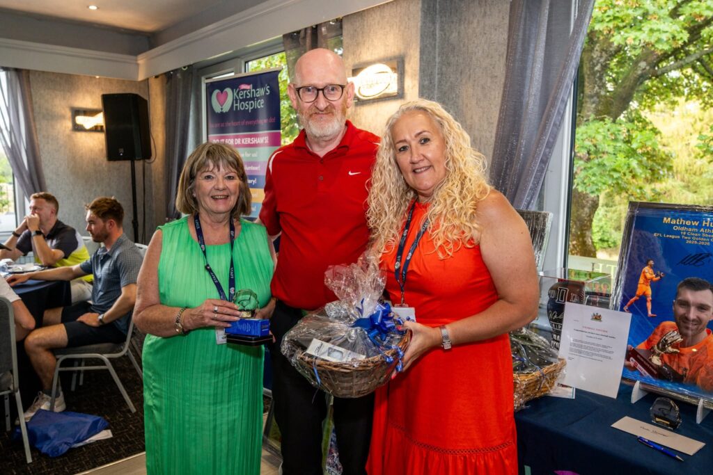 Two members of Dr Kershaw's staff smiling and presenting a man wearing a red t-shirt with a prize