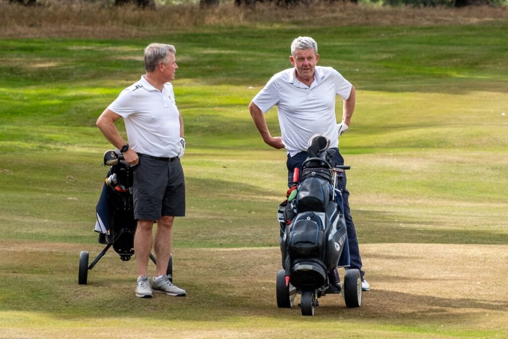 Two men wearing white shirts with their buggies on the golf course
