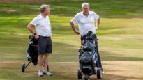 Two men wearing white shirts with their buggies on the golf course