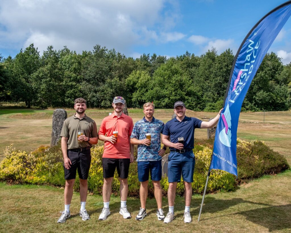 Four men holding a Dr Kershaw's Hospice flag on a grassy golf course