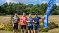 Four men holding a Dr Kershaw's Hospice flag on a grassy golf course