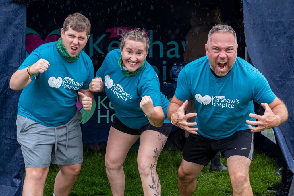 Two men and one women posing in Dr Kershaw's Hospice t-shirts, covered in mud