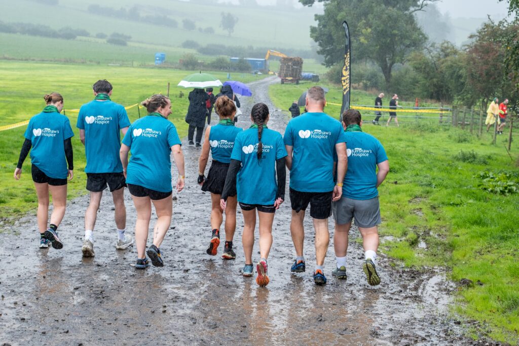 A group of people in blue Dr Kershaw's Hospice t-shirts walking away through a muddy field