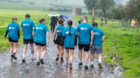 A group of people in blue Dr Kershaw's Hospice t-shirts walking away through a muddy field