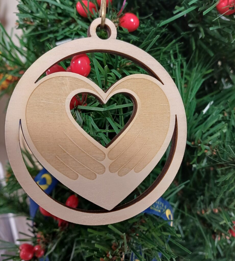 Light Up a Life 2025 bauble: natural wood engraved circle with cut out detail of two hands in the shape of a heart
