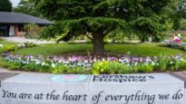 A sea of lilac Rose to Remember roses behind a wall with the Dr Kershaw's Hospice logo, 'You are at the heart of everything we do!'