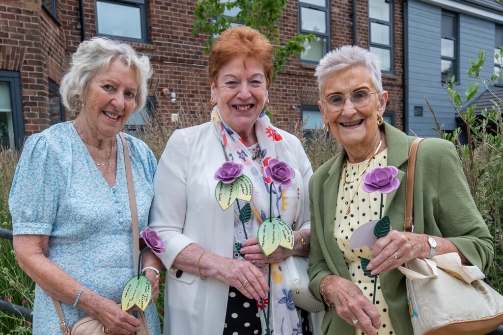 Three women holding their lilac roses outside the hospice