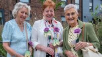 Three women holding their lilac roses outside the hospice