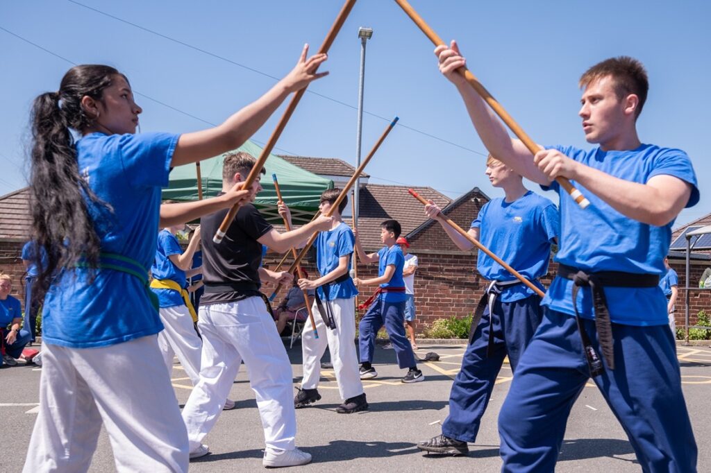 Children dressed in blue holding up sticks