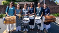 A group of smartly dressed Asian women holding drums