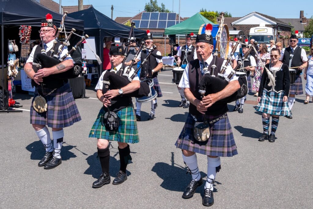 A crowd of men in kilts playing the bagpipes as they walk towards Dr Kershaw's Hospice