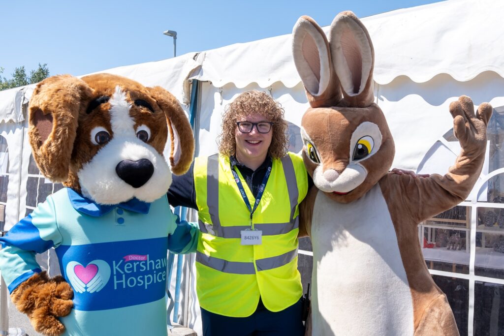 Dr Kershaw's Hospice's mascot, Hartley the dog, standing with a staff member in a high-vis jacket and a life-size Peter Rabbit bunny