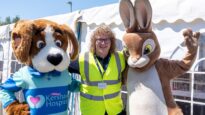 Dr Kershaw's Hospice's mascot, Hartley the dog, standing with a staff member in a high-vis jacket and a life-size Peter Rabbit bunny