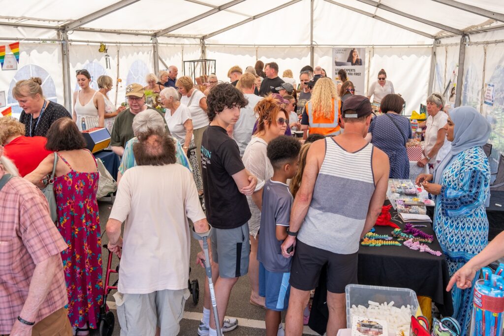 A busy crowd of people looking at stalls inside a white marquee