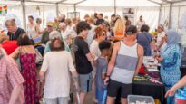 A busy crowd of people looking at stalls inside a white marquee
