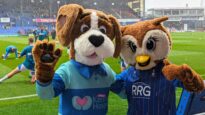 Hartley the dog and Chaddy the owl in front of the Oldham Athletic football pitch