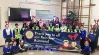 Children in a school hall with a large sign saying 'Thank you to all our Reindeer Runners'