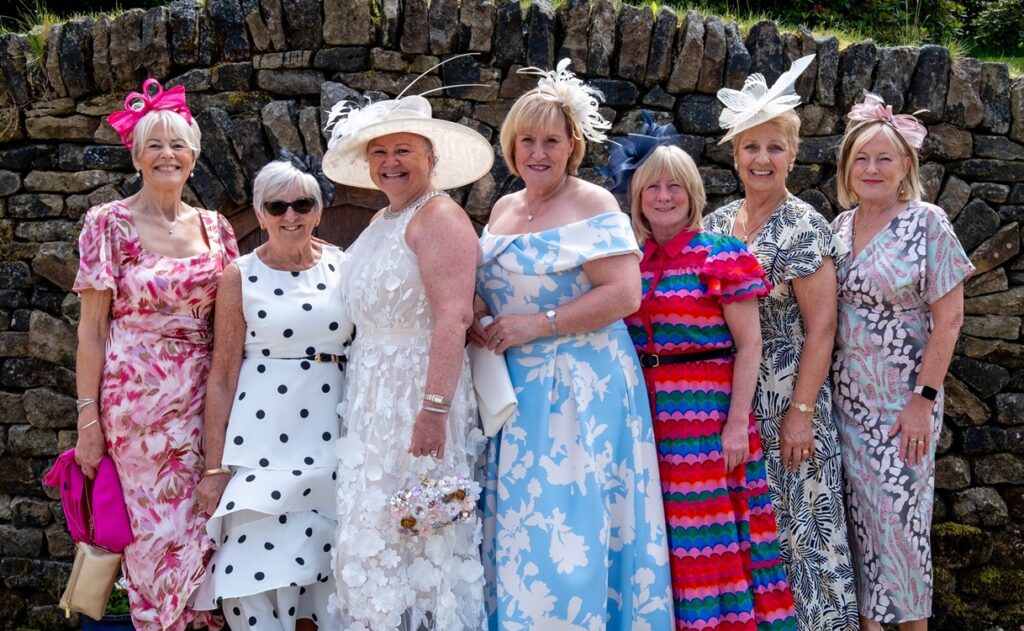 Seven women standing in a row, wearing colourful dresses