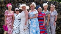 Seven women standing in a row, wearing colourful dresses