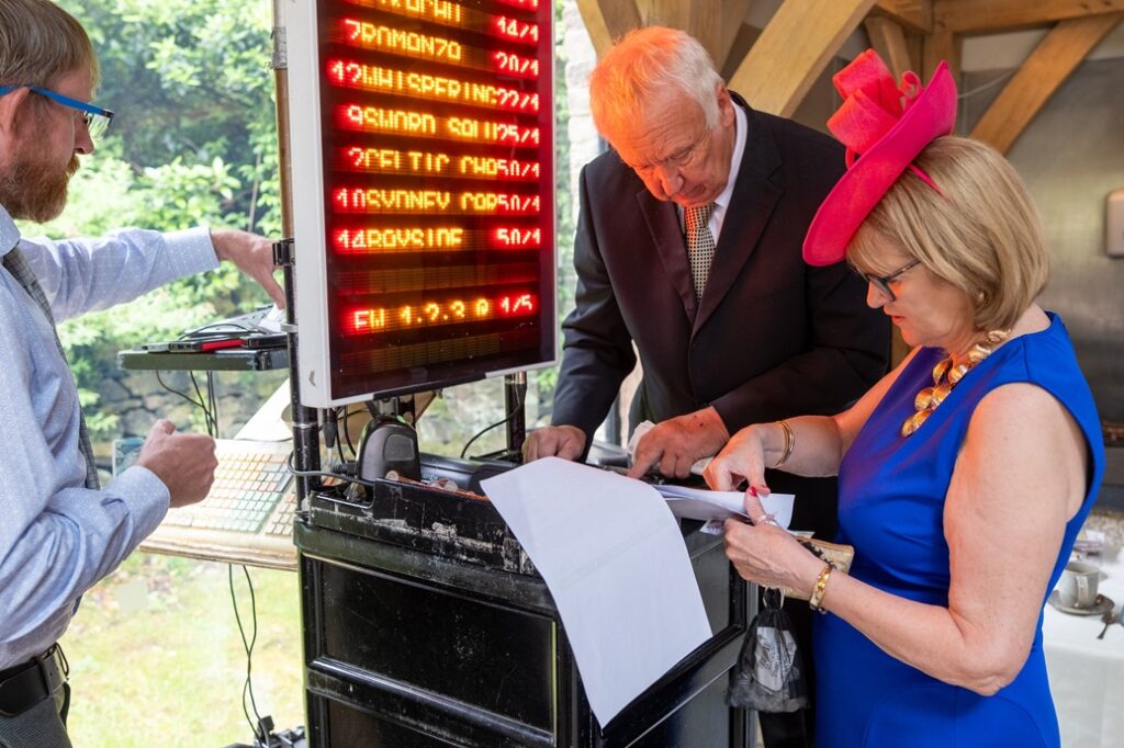 A DJ with a woman wearing a cobalt dress and pink fascinator