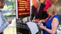 A DJ with a woman wearing a cobalt dress and pink fascinator